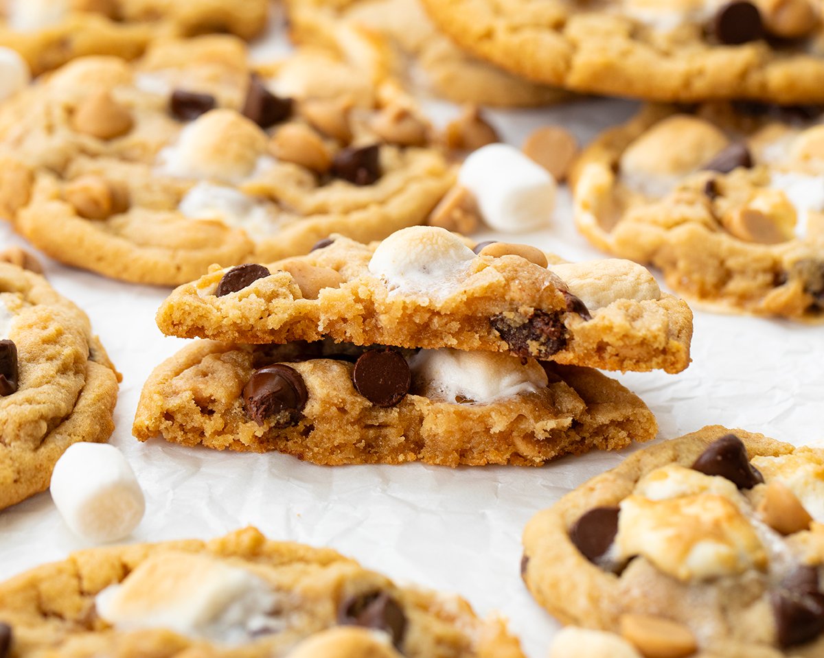 Soft, chewy peanut butter marshmallow cookies loaded with melty chocolate chips and gooey marshmallows. Easy, delicious, and perfect for any cookie lover! Broken in half Peanut Butter Marshmallow Cookies on a white table.