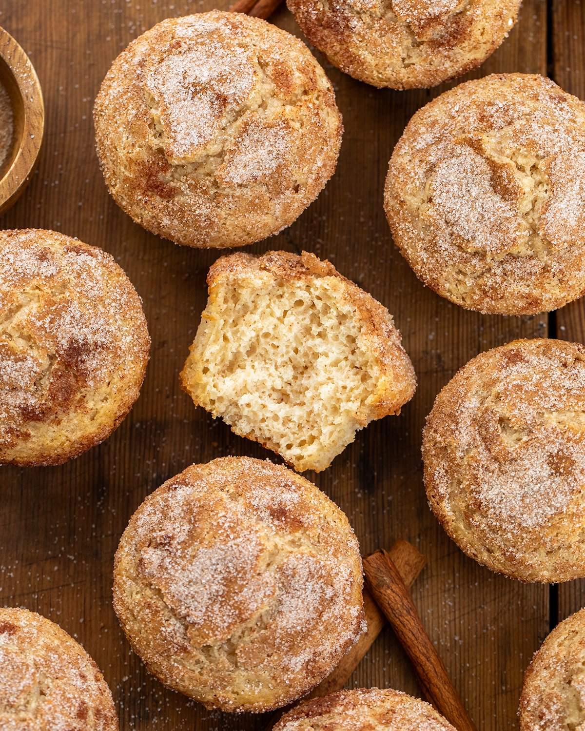 These Snickerdoodle Muffins are soft, tender cinnamon-sugar muffins with the classic tang from Snickerdoodle Cookies. They're inspired by my popular cinnamon sugar donut muffins but with that signature Snickerdoodle twist! Snickerdoodle Muffins on a wooden table with the center muffin cut in half showing inside texture.