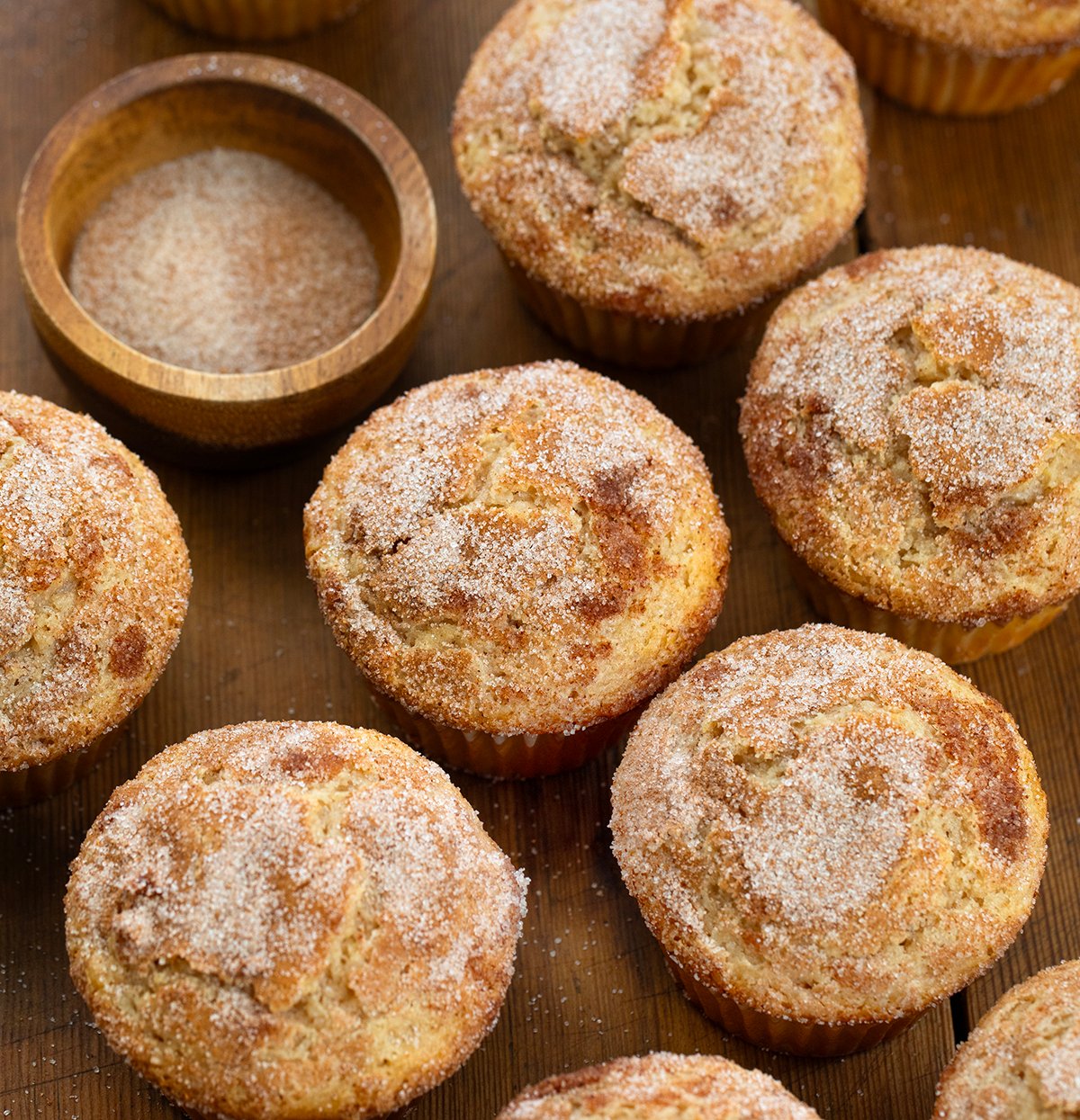 These Snickerdoodle Muffins are soft, tender cinnamon-sugar muffins with the classic tang from Snickerdoodle Cookies. They're inspired by my popular cinnamon sugar donut muffins but with that signature Snickerdoodle twist! Snickerdoodle Muffins on a wooden table with cinnamon sugar.
