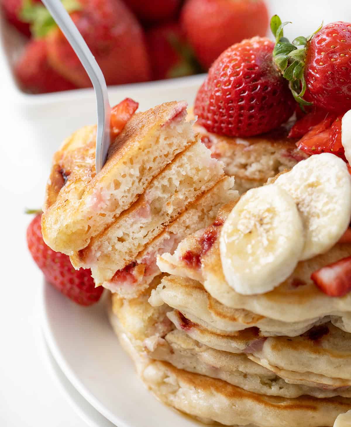 These Strawberry Banana Pancakes are a fruit-filled twist on my classic buttermilk pancakes. Fresh strawberries and mashed bananas are folded right into the batter, making every bite tender, light, and full of flavor! Fork picking up a bite of Strawberry Banana Pancakes.