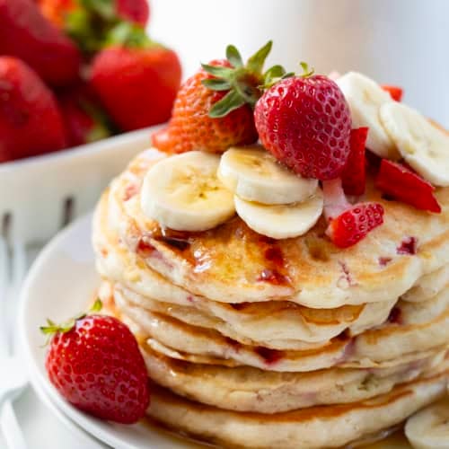 Close up of the top of a stack of Strawberry Banana Pancakes with fresh strawberries and banana slices.