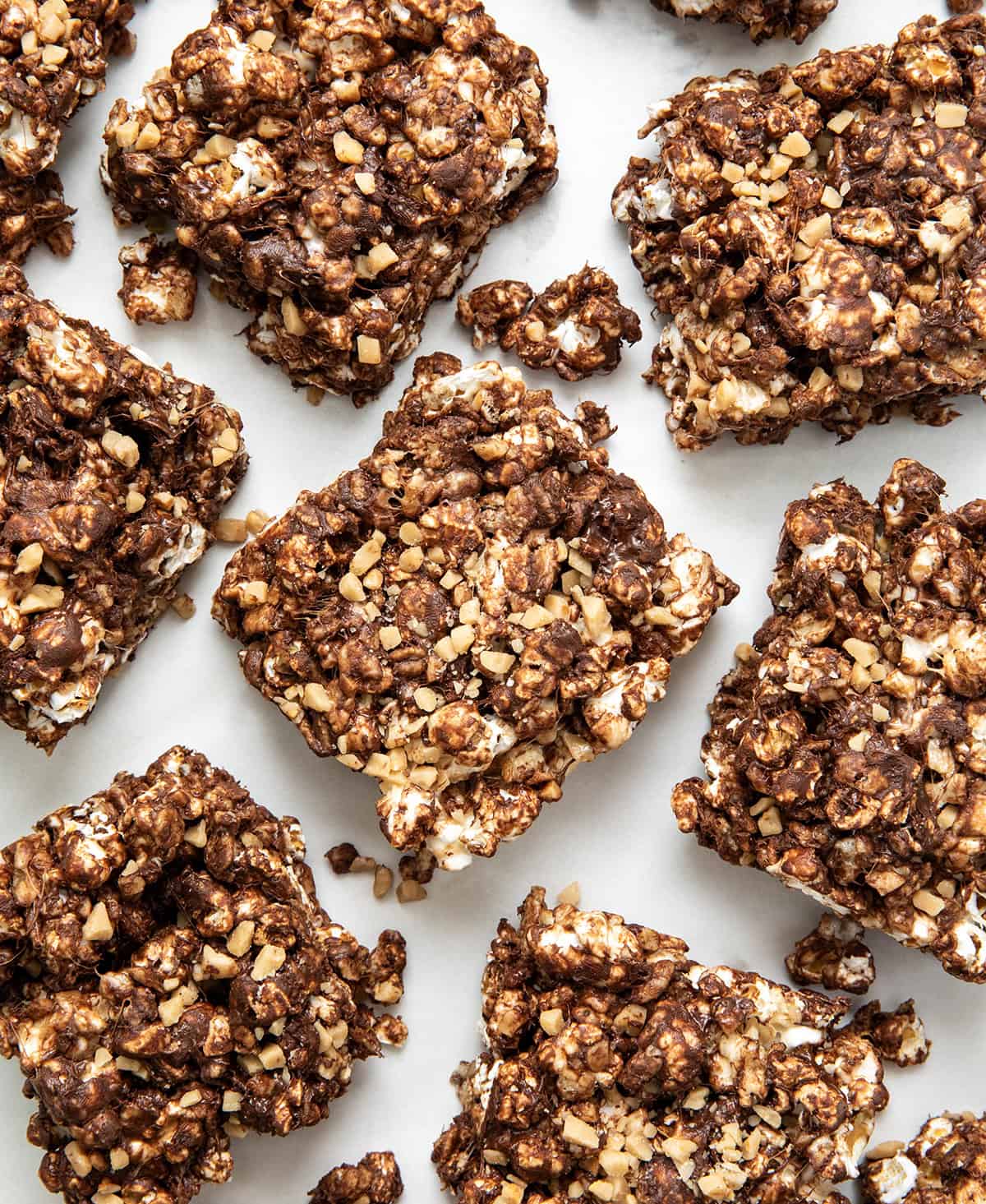These Toffee Crunch Popcorn Bars are one of my go-to treats when I want something sweet, quick, and a little bit extra. They are made with crispy rice cereal, gooey marshmallows, rich chocolate, and a sprinkle of toffee for that perfect sweet crunch. Toffee Crunch Popcorn Bars cut into squares on a white table from overhead.