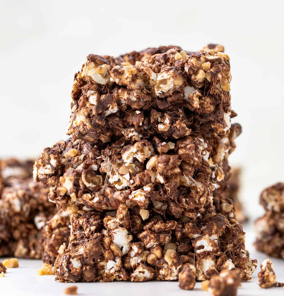 These Toffee Crunch Popcorn Bars are one of my go-to treats when I want something sweet, quick, and a little bit extra. They are made with crispy rice cereal, gooey marshmallows, rich chocolate, and a sprinkle of toffee for that perfect sweet crunch. Stack of three Toffee Crunch Popcorn Bars on a white table.