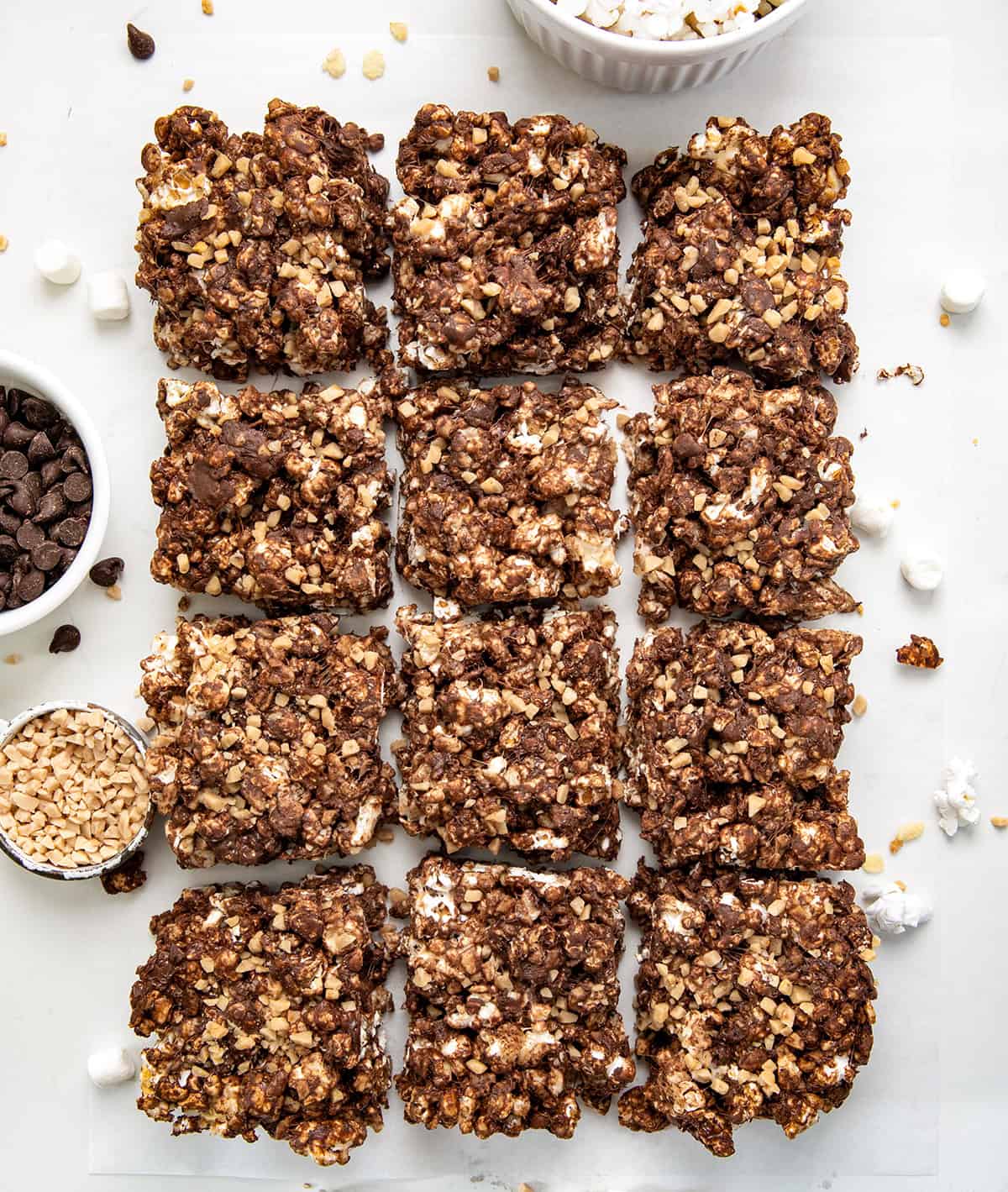 These Toffee Crunch Popcorn Bars are one of my go-to treats when I want something sweet, quick, and a little bit extra. They are made with crispy rice cereal, gooey marshmallows, rich chocolate, and a sprinkle of toffee for that perfect sweet crunch. Toffee Crunch Popcorn Bars cut into squares on a white table from overhead.