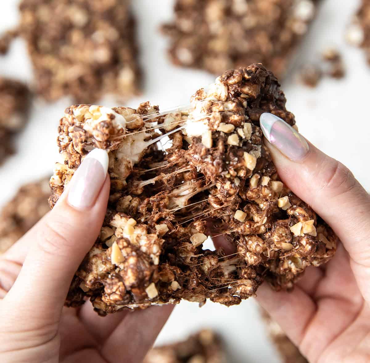 These Toffee Crunch Popcorn Bars are one of my go-to treats when I want something sweet, quick, and a little bit extra. They are made with crispy rice cereal, gooey marshmallows, rich chocolate, and a sprinkle of toffee for that perfect sweet crunch. Hands breaking apart a Toffee Crunch Popcorn Bar.