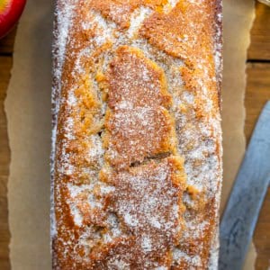 Loaf of Apple Cider Donut Bread on a wooden table with fresh apples and apple cider.
