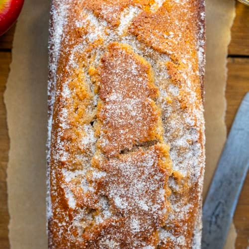 Loaf of Apple Cider Donut Bread on a wooden table with fresh apples and apple cider.