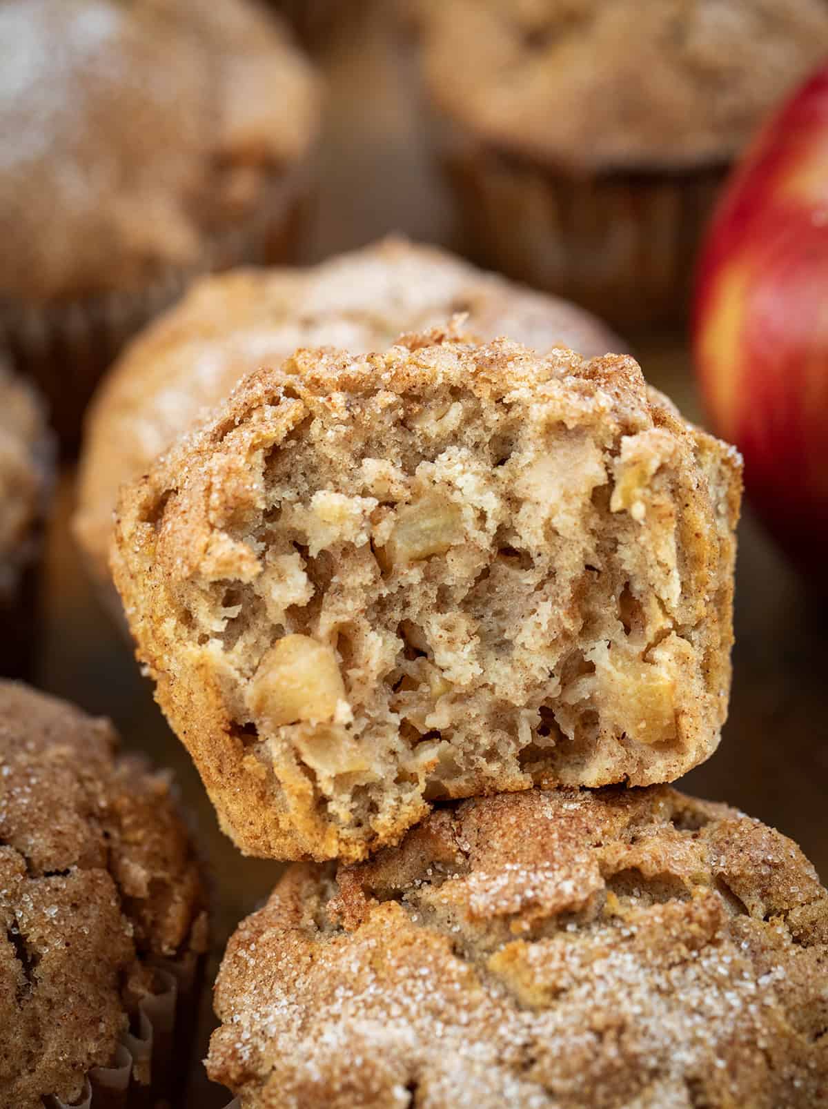 These Apple Snickerdoodle Muffins are soft, fluffy, and full of cozy fall flavor with apples, warm spice, and a buttery cinnamon-sugar topping. Perfect for breakfast, brunch, or snacking! Apple Snickerdoodle Muffin that has been halved and is resting on other muffins.