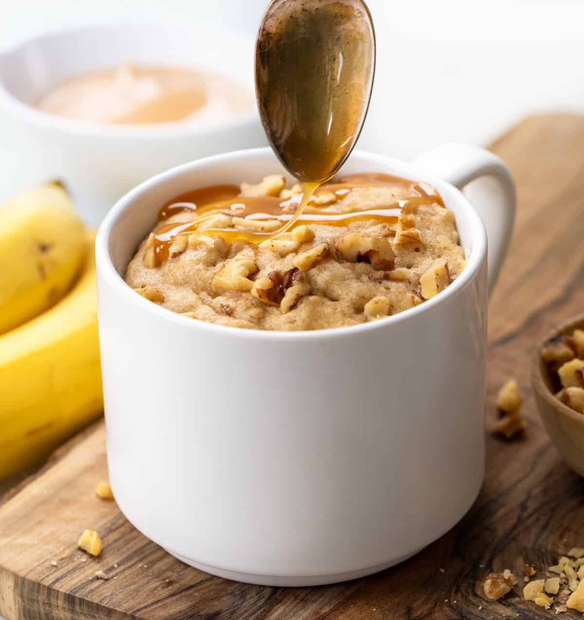 Drizzling caramel over Banana Nut Mug Cake in a white mug.