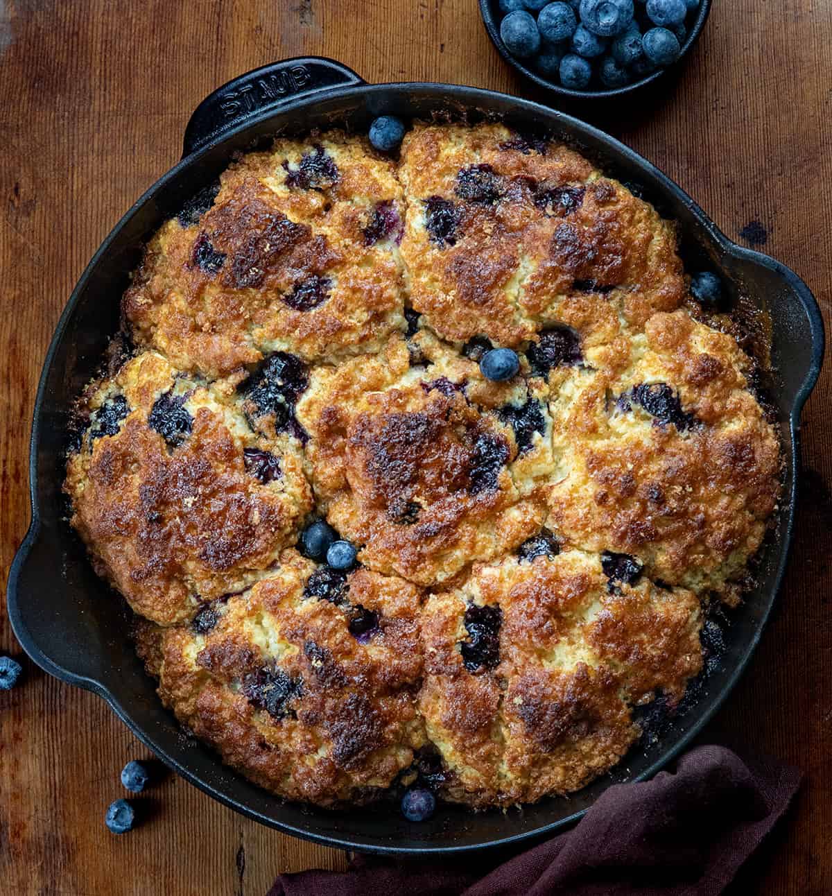 Skillet of Blueberry Cinnamon Crunch Cathead Biscuits on a wooden table from overhead.