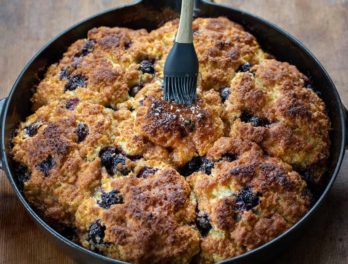 Brushing melted butter over Blueberry Cinnamon Crunch Cathead Biscuits.