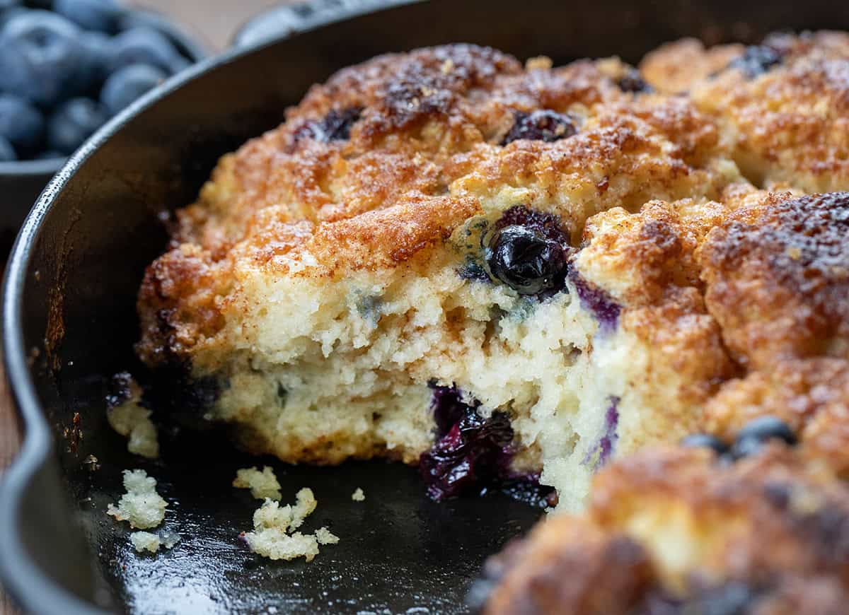 Blueberry Cinnamon Crunch Cathead Biscuits in a skillet with some biscuits removed and showing tender crumb.