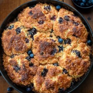 Skillet of Blueberry Cinnamon Crunch Cathead Biscuits on a wooden table from overhead.