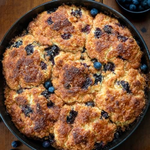 Skillet of Blueberry Cinnamon Crunch Cathead Biscuits on a wooden table from overhead.