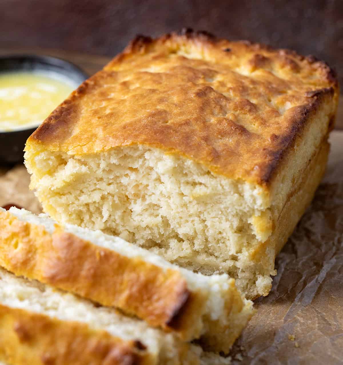 This Butter Swim Bread is golden, buttery, and irresistibly tender because it bakes right in a pool of melted butter. The butter gives the loaf crisp edges, a rich flavor, and a soft, biscuit-like crumb that melts in your mouth! Loaf of Butter Swim Bread on a wooden table with some melted butter.