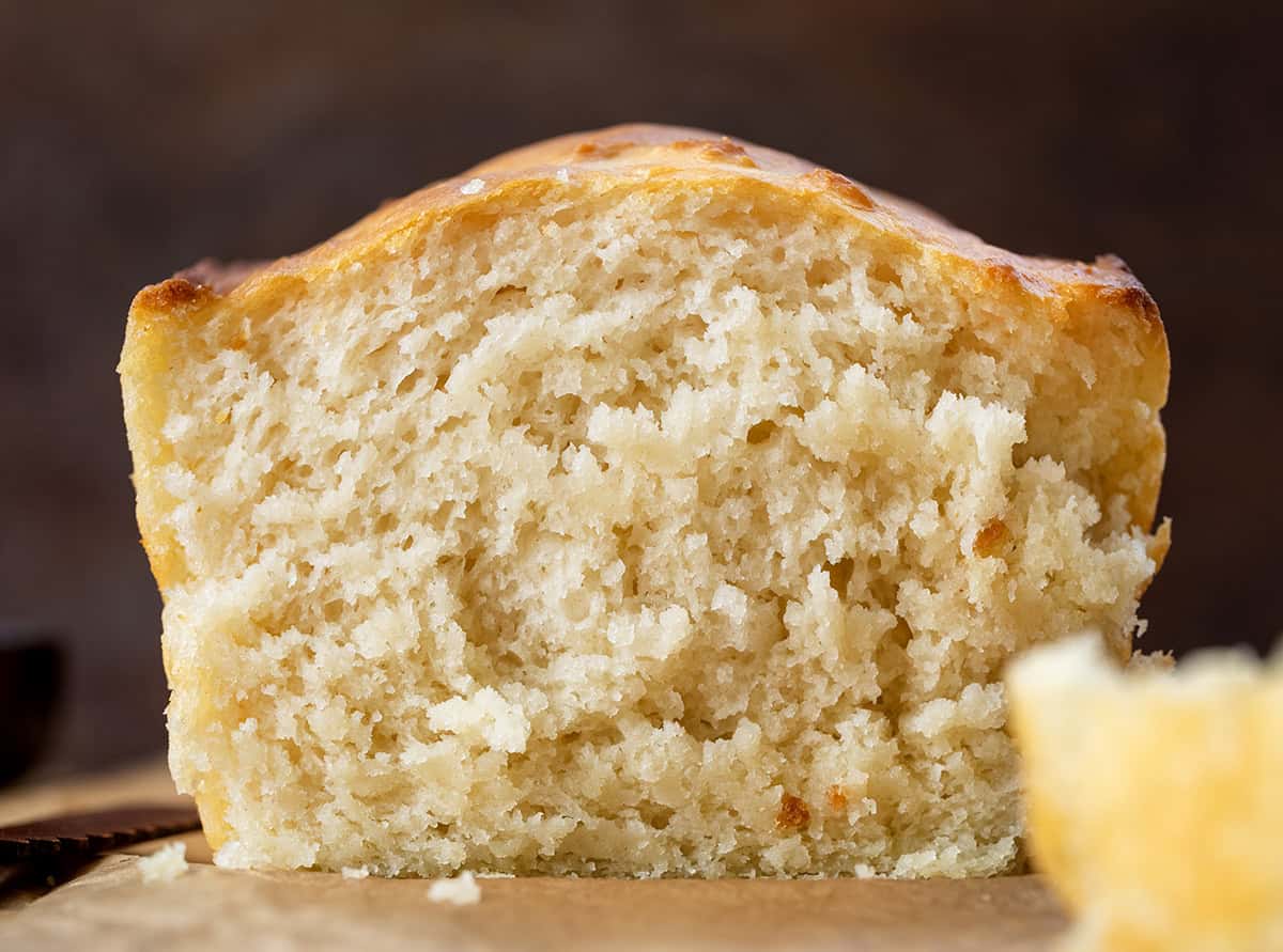 This Butter Swim Bread is golden, buttery, and irresistibly tender because it bakes right in a pool of melted butter. The butter gives the loaf crisp edges, a rich flavor, and a soft, biscuit-like crumb that melts in your mouth! Loaf of Butter Swim Bread on a wooden table with some cut away showing inside texture.