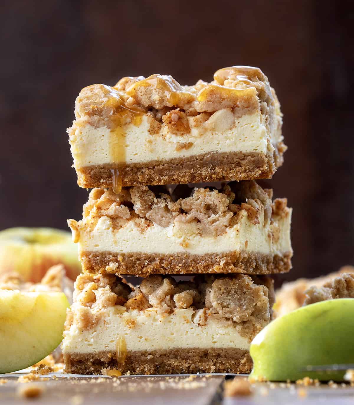 Stack of Caramel Apple Cheesecake Bars on a wooden table with fresh apples.