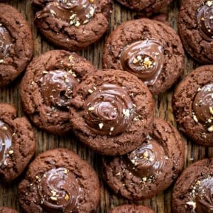 Chocolate Hazelnut Thumbprint Cookies on a wooden table with a couple of the cookies stacked.