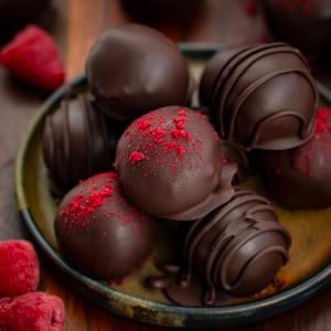 Close up of Chocolate Raspberry Truffles on a plate with fresh raspberries.