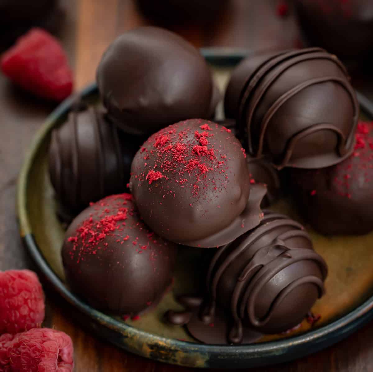 If you love the bold pairing of chocolate and raspberries, these Chocolate Raspberry Truffles are a treat youโll want to make again and again! Close up of Chocolate Raspberry Truffles on a plate with fresh raspberries.