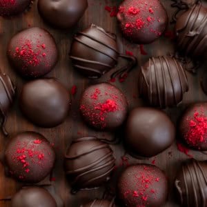 Chocolate Raspberry Truffles on a wooden table some with dried raspberry, some with chocolate lines, some plain from overhead.