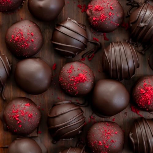 Chocolate Raspberry Truffles on a wooden table some with dried raspberry, some with chocolate lines, some plain from overhead.