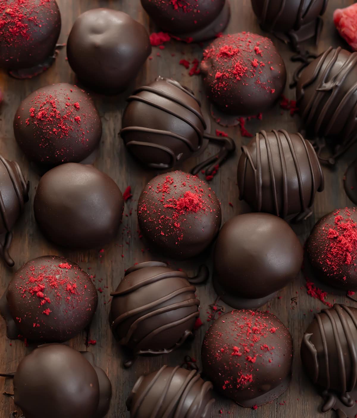 If you love the bold pairing of chocolate and raspberries, these Chocolate Raspberry Truffles are a treat youโll want to make again and again! Chocolate Raspberry Truffles on a wooden table some with dried raspberry, some with chocolate lines, some plain from overhead.