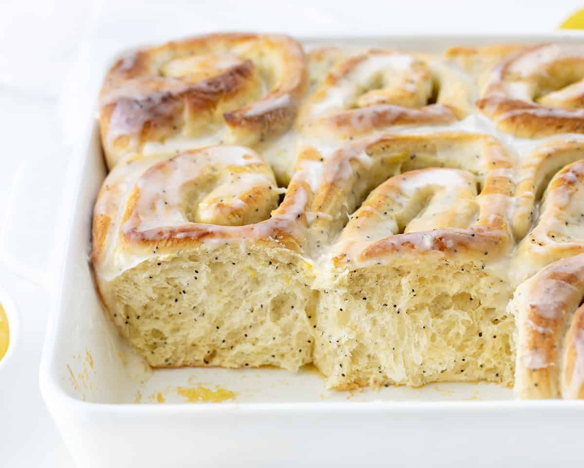 These Lemon Poppy Seed Rolls are soft, fluffy, sweet rolls filled with tangy lemon curd and topped with a light glaze that soaks into every bite! Lemon Poppy Seed Rolls in the pan with a couple of rolls removed.