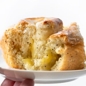 Hand holding a white plate with a Lemon Poppy Seed Roll on it.