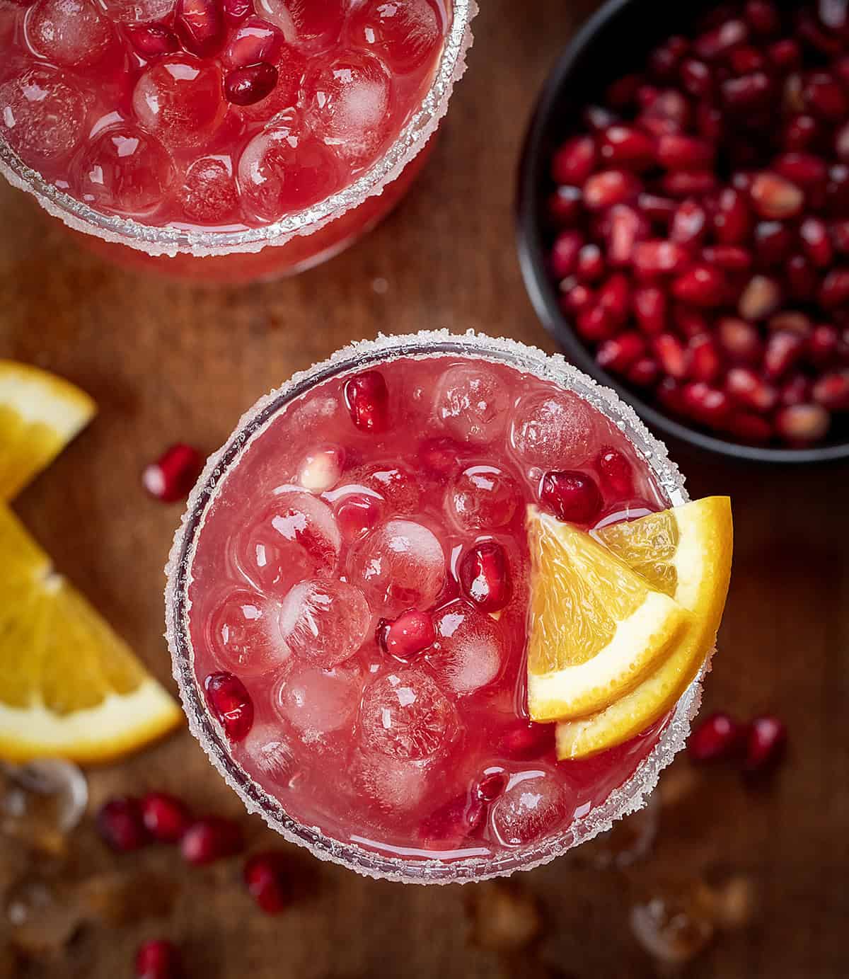 Looking down on glasses of Orange Pomegranate Margarita on a wooden table.