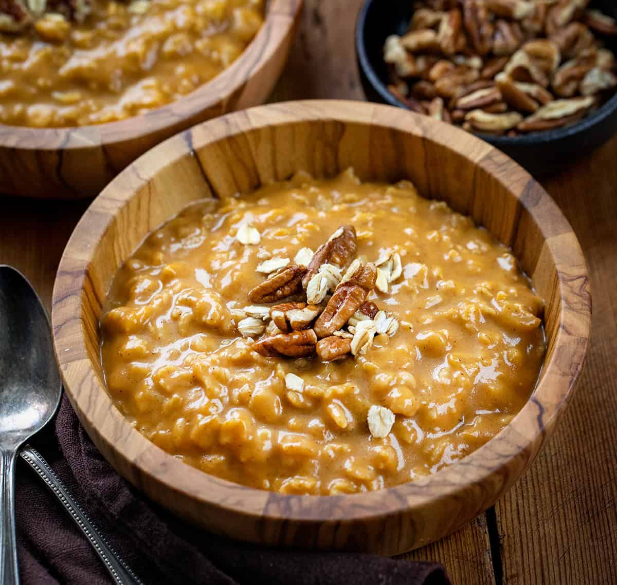 Bowl of Pumpkin Spice Oatmeal on a wooden table with a spoon next to it and a bowl of pecans.