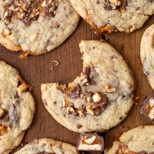 Snickers Cookies on a wooden table with one cookie missing a bite.