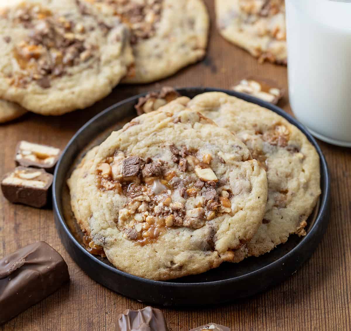 Snickers Cookies on a small black plate on a wooden table with milk.
