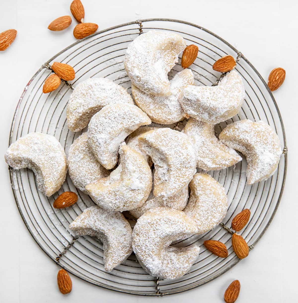 There’s something magical about these delicate almond crescent cookies. They’re buttery, tender, and melt-in-your-mouth soft, with just the right dusting of sweet confectioners’ sugar! Wire rack of Almond Crescent Cookies with almonds.
