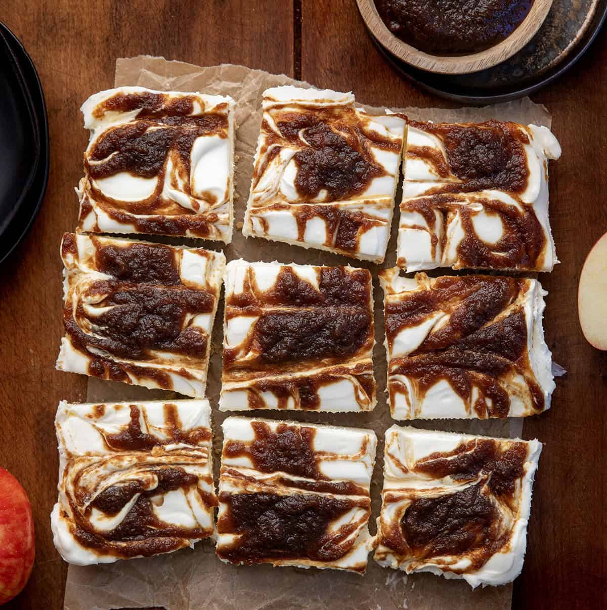 If you love my Apple Butter Cheesecake, you’re going to adore these Apple Butter Cheesecake Bars! With a buttery graham cracker crust, fluffy cream cheese filling, and swirls of sweet apple butter, these bars are perfectly rich, yet so light! Apple Butter Cheesecake Bars cut into squares on a wooden table from overhead.
