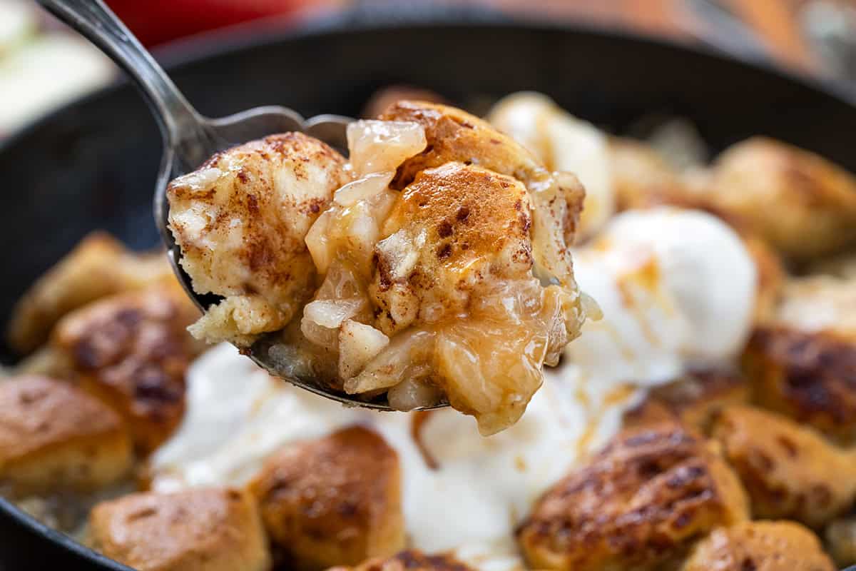 This 2-Ingredient Apple Cinnamon Roll Bake is effortless, cozy, and perfect for a snack, brunch, or dessert! Using store-bought cinnamon rolls and sweet apple pie filling, this bake comes together in just minutes but tastes like a homemade treat. Scoop of Apple Cinnamon Roll Bake held above the skillet.