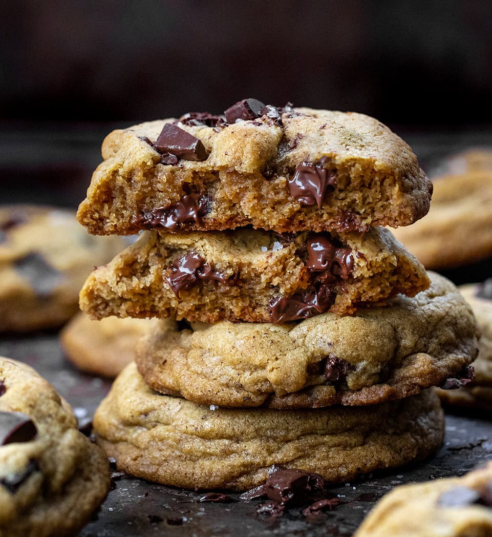 These Browned Butter Pumpkin Chocolate Chip Cookies are soft, chewy, and bursting with cozy fall flavors. The nutty richness of browned butter pairs perfectly with pumpkin and pumpkin pie spice, while melty chocolate chunks add indulgence in every bite! Stack of Browned Butter Pumpkin Chocolate Chip Cookies with top cookie broken in half showing melted chocolate and tender crumb.
