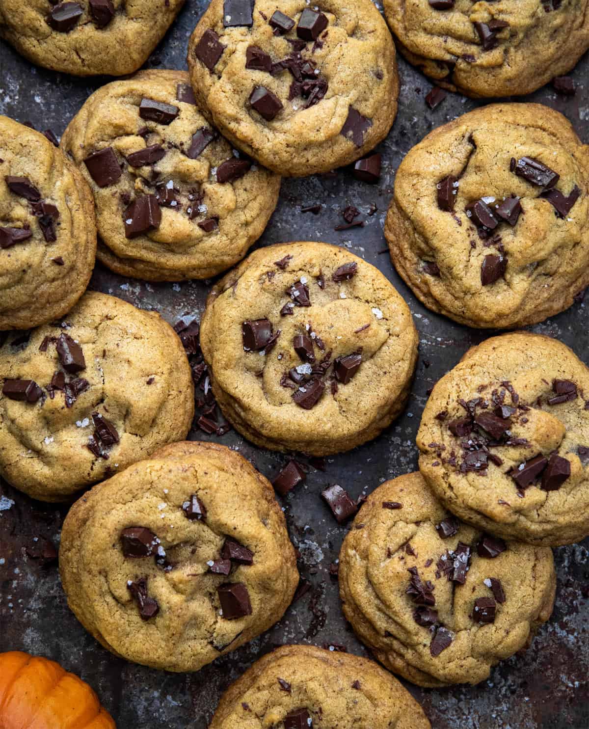Browned Butter Pumpkin Chocolate Chip Cookies on a dark table with a mini pumpkin from overhead.