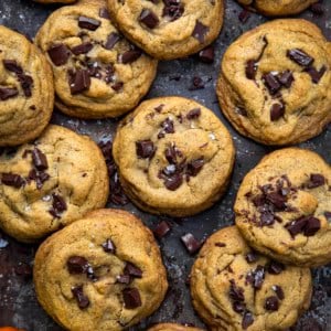 Browned Butter Pumpkin Chocolate Chip Cookies on a dark table with a mini pumpkin from overhead.