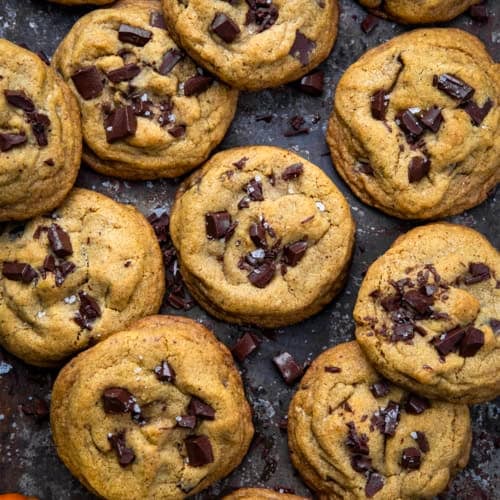 Browned Butter Pumpkin Chocolate Chip Cookies on a dark table with a mini pumpkin from overhead.