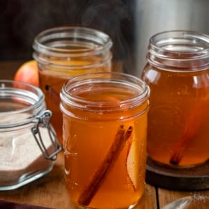 Crock Pot Apple Cider in mason jars on a wooden table.