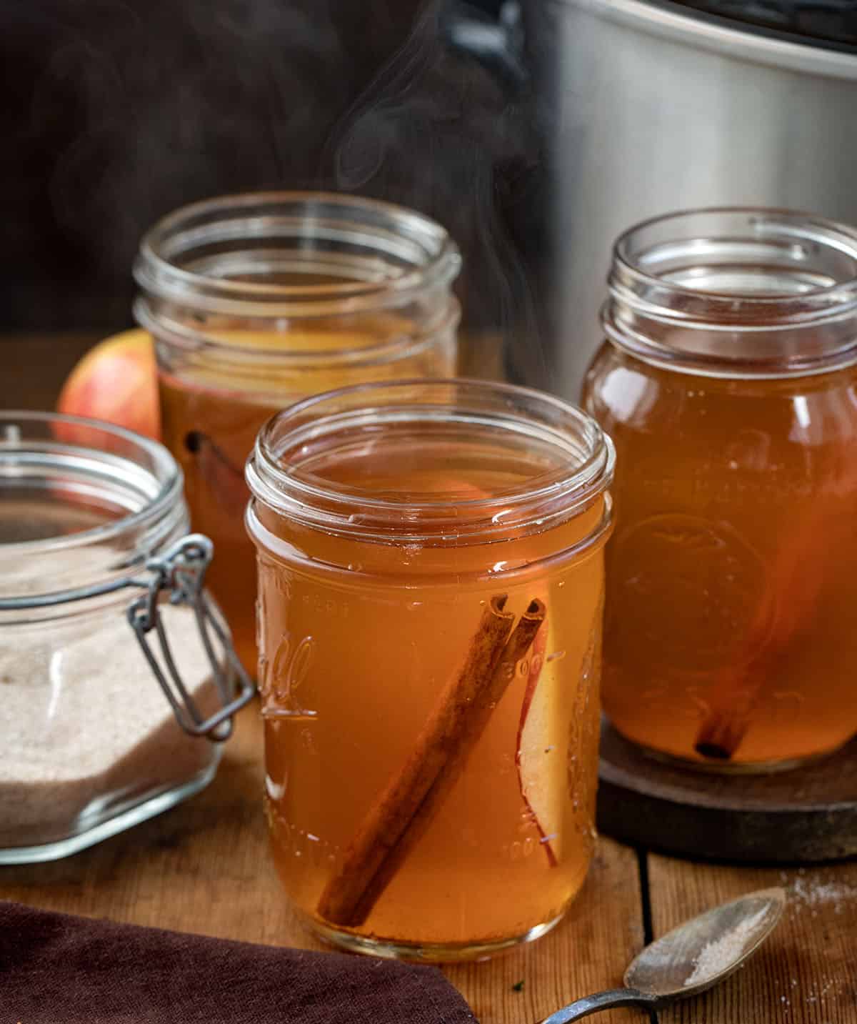 Crock Pot Apple Cider in mason jars on a wooden table.