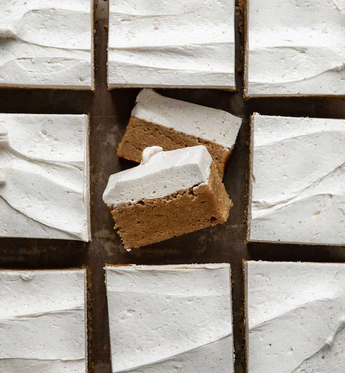 These Frosted Gingerbread Brownies start with my beloved gingerbread brownie base and get a decadent upgrade with a creamy gingerbread ermine frosting. The brownies are soft, tender, and perfectly spiced, while the frosting adds a silky, sweet layer that melts in your mouth! Frosted Gingerbread Brownies cut into squares and one brownie cut into smaller pieces and on its side from overhead.