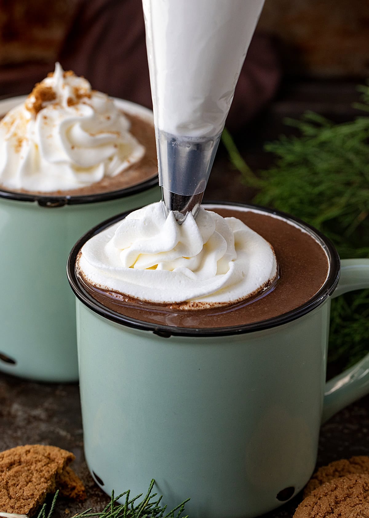 Piping whipped cream onto a Gingerbread Hot Chocolate.