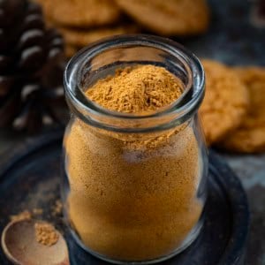 Jar of Gingerbread Spice Mix on a black plate with a small measuring spoon next to it.