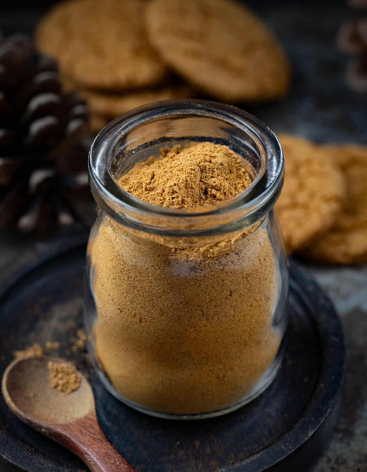 Warm up your winter baking with my special Gingerbread Spice Mix! A cozy, homemade blend that instantly makes your kitchen smell like the holidays. This easy mix captures all the nostalgic flavor of classic gingerbread in one jar! Jar of Gingerbread Spice Mix on a black plate with a small measuring spoon next to it.