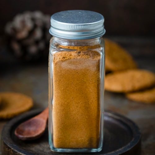 Jar of Gingerbread Spice Mix on a black plate on a wooden table.
