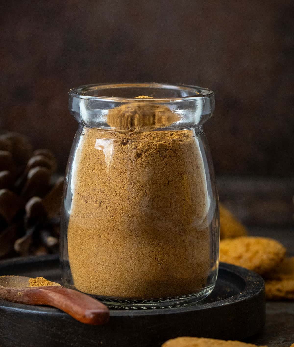 Warm up your winter baking with my special Gingerbread Spice Mix! A cozy, homemade blend that instantly makes your kitchen smell like the holidays. This easy mix captures all the nostalgic flavor of classic gingerbread in one jar! Mini jar of Gingerbread Spice Mix on a black plate on a wooden table close up.