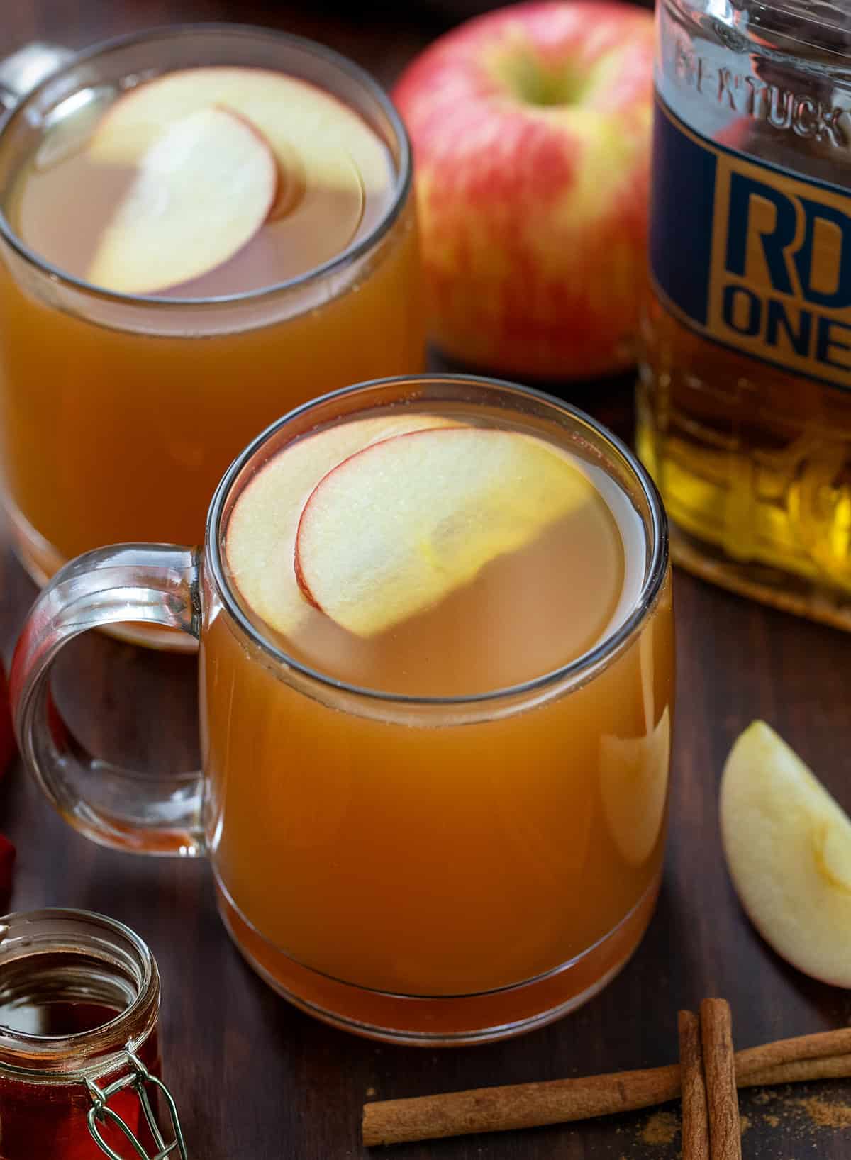 Glass mugs of Maple Bourbon Apple Cider with bourbon, maple syrup, and fresh apples.
