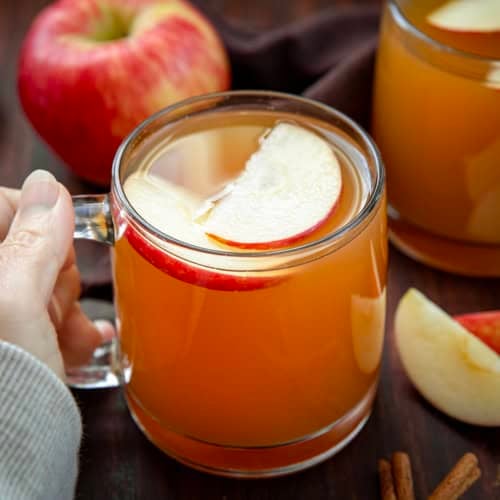 Hand holding a mug of Maple Bourbon Apple Cider on a wooden table.